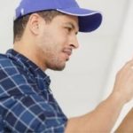 Technician in blue cap working on a thermostat, representing Charles Krull & Son, Inc.