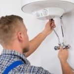 Male technician repairing a water heater with tools, demonstrating plumbing services by Charles Krull & Son, Inc.