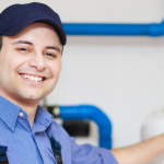 Male plumber in blue cap and shirt smiling, with plumbing tools and blue pipes, focusing on water heater services.