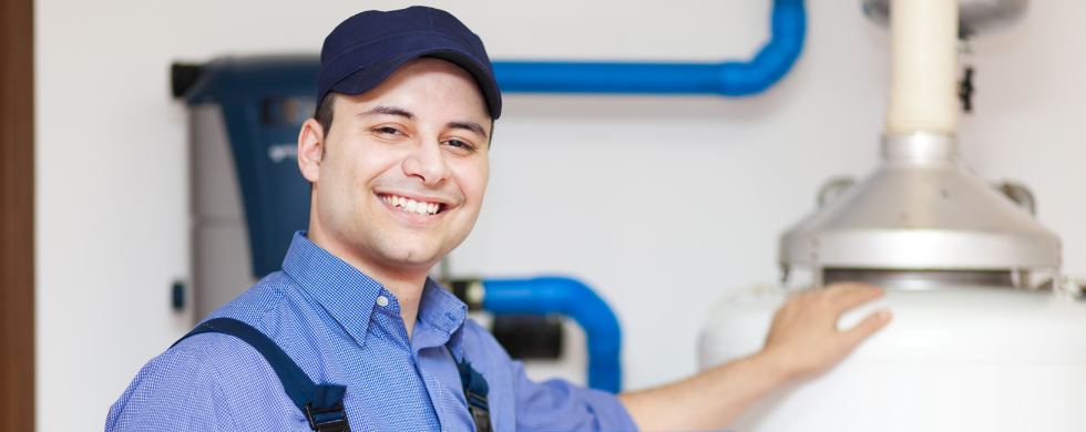 Smiling male technician in blue cap servicing a water heater for plumbing by Charles Krull & Son, Inc.
