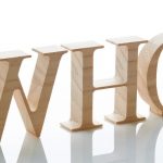 Three-dimensional wooden letters spelling "WHO," representing inquiry and Lillian Baumbach's plumbing legacy.