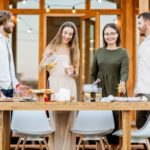 Four young adults gather around a wooden table with food and drinks, enjoying a casual social event.