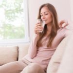 Young woman relaxing on a neutral sofa, holding a glass of water, emphasizing the benefits of filtered water at home.
