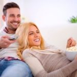 Couple on a couch watching TV, enjoying popcorn, highlighting festive 4th of July celebrations with plumbing tips.