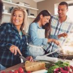 Three people in a modern kitchen preparing vegetables for 4th of July cooking.