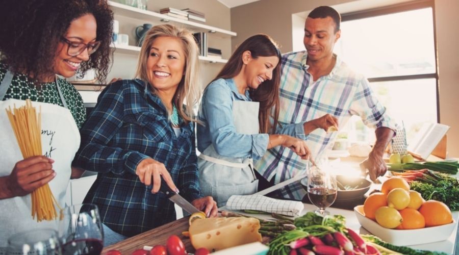 Four friends cooking in a bright kitchen with fresh ingredients and tools, promoting collaboration in culinary experiences.