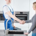 Plumber in blue overalls shakes hands with female client in modern kitchen, showcasing Charles Krull & Son, Inc. services.
