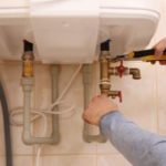 Plumber installing a white sink with pipe connections and fittings for home maintenance by Charles Krull & Son, Inc.