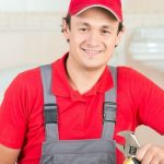 Smiling plumber in red cap and shirt, holding a wrench in a home workspace, representing Charles Krull & Son, Inc. services.