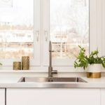 Modern kitchen sink with stainless steel fixtures, natural light, and potted plants by Charles Krull & Son, Inc.