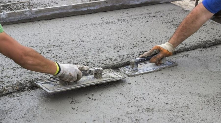 Two construction workers applying freshly poured concrete with trowels for plumbing and heating installation.