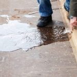 Individual cleaning a water spill on a wet floor, indicating slab leak issues from Charles Krull & Son, Inc.