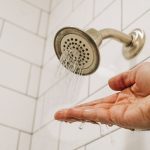 Stainless steel showerhead with water droplets on white bathroom tiles, showcasing plumbing solutions for low water pressure.