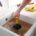 Plumber using a plunger to clear a sink with dirty water; Charles Krull & Son, Inc. services plumbing blockage solutions.