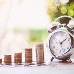 Classic alarm clock next to stacked coins, symbolizing financial planning and savings for plumbing solutions.