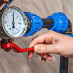 Hand adjusting brightly colored valve handle near pressure gauge, highlighting plumbing service by Charles Krull & Son, Inc.