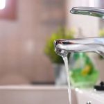 Shiny faucet with running water above a sink, illustrating plumbing and heating solutions for low water pressure issues.