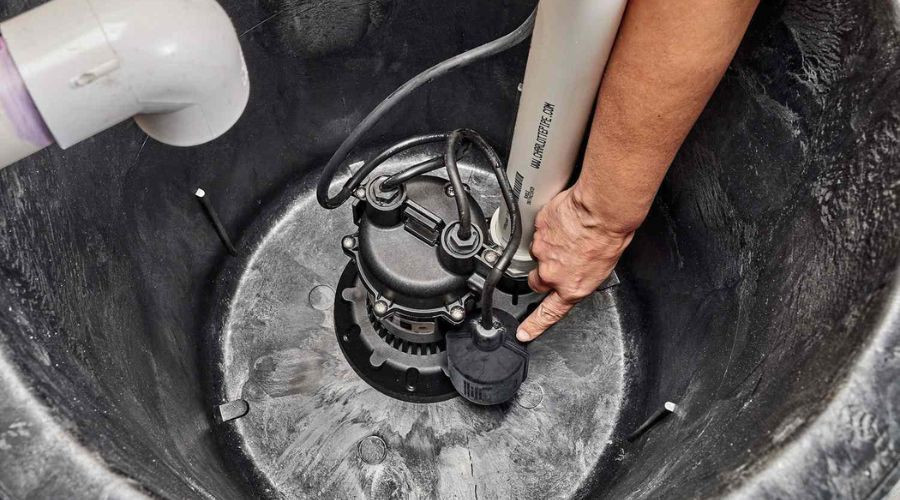 Human hand adjusting a sump pump in a dark pit, part of plumbing maintenance by Charles Krull & Son, Inc.