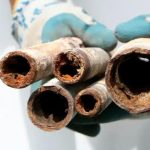 Close-up of a hand in gloves holding corroded pipes, illustrating plumbing maintenance issues for Charles Krull & Son, Inc.