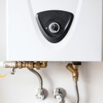 White wall-mounted water heater with control knob and pipes, representing plumbing services by Charles Krull & Son, Inc.