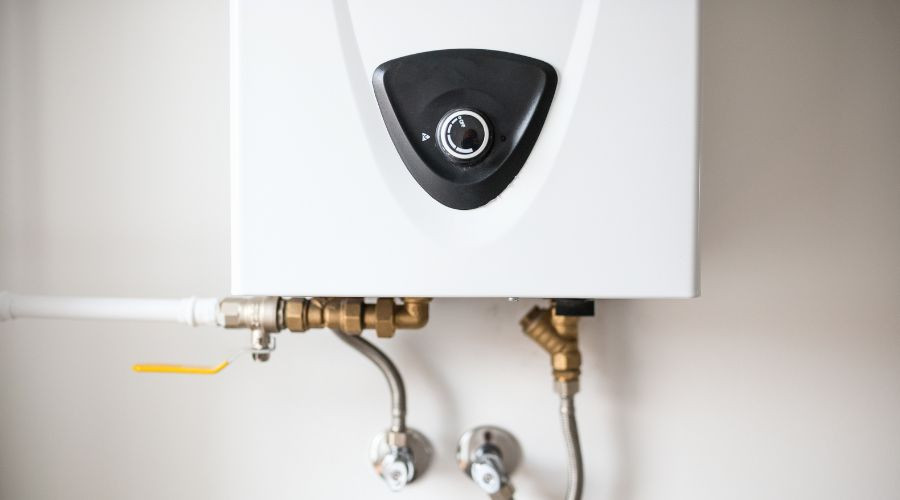 Wall-mounted water heater with black control knob, metal pipes, and valves from Charles Krull & Son, Inc. Plumbing & Heating.