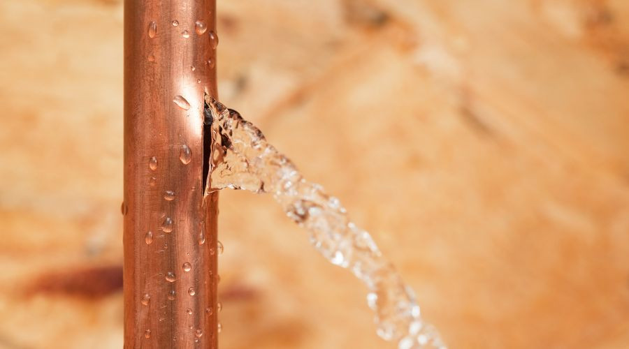 Copper pipe leaking water with droplets, illustrating water leak detection services for plumbing issues.