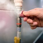 Hand adjusting a gas line connection with visible steam, emphasizing gas leak detection and safety in plumbing services.
