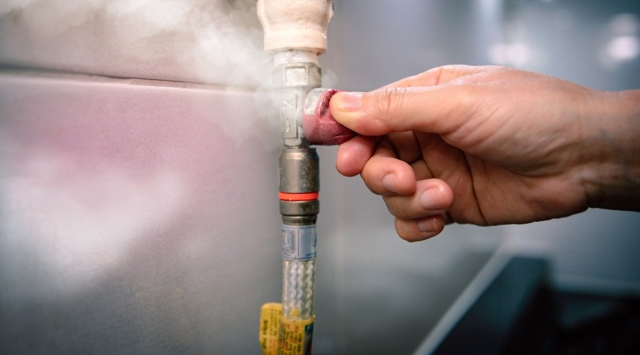 Hand adjusting a plumbing valve with steam visible, illustrating water leak detection and prevention techniques relevant to plumbing services.